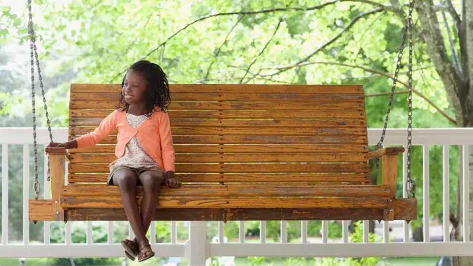 A little girl sitting on a porch swing