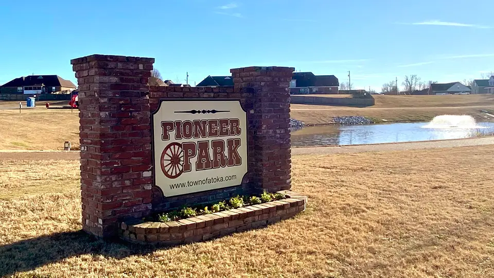 The Pioneer Park sign near a pond that is close to Mini Mall Storage 