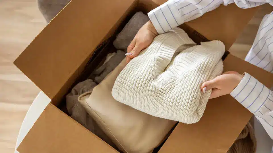 neutral toned sweaters being packed into a moving box for storage with Mini Mall Storage